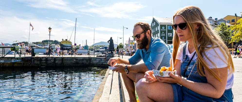 Par som sitter på kaikanten og spiser fish and chips fra Fishan i Kristiansund. Foto. 