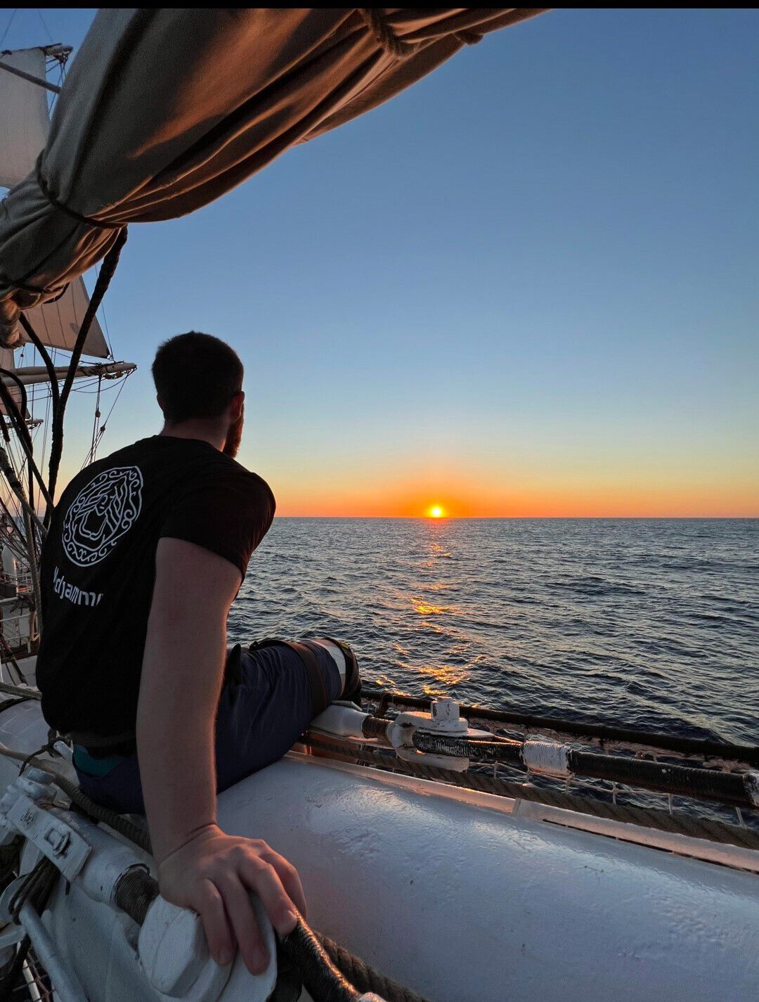 bilde av person på seilskute ryggen til ser utover solnedgang