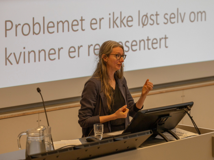 Liv Bjørnhaug Johansen på talerstol, med en tekst på skjerm bak: Problemet er ikke løst selv om kvinner er representert