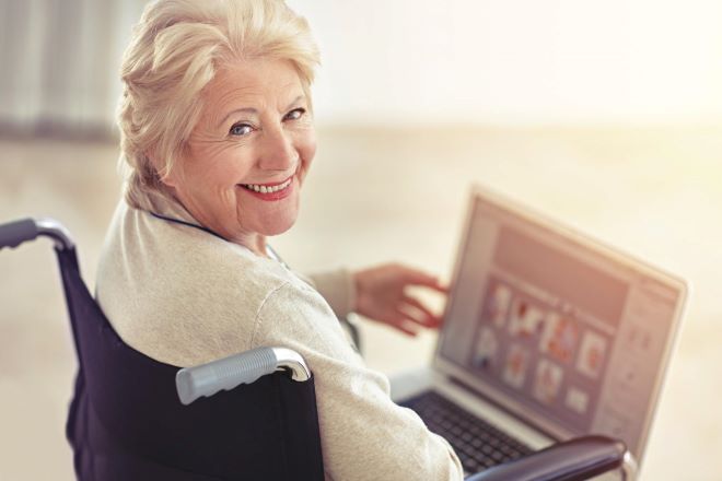 Illustrasjonsfoto av eldre dame i rullestol med PC-skjerm i fanget